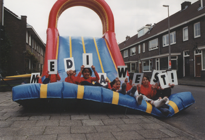 605950 Afbeelding van buurtkinderen die vanaf een glijbaan de letters MEDIA WEST! omhoog houden in de Van Meursstraat ...